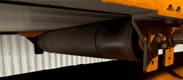 Close-up view of a cylindrical roller or conveyor belt mechanism attached to a metal structure, with a corrugated metal background.