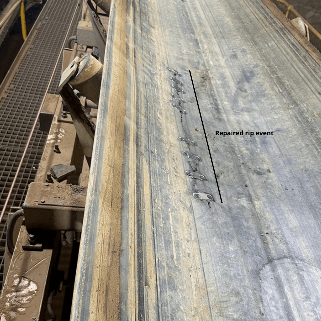 Conveyor belt with a visible repaired rip, indicated by a label "Repaired rip event." The belt surface shows wear and machinery is partially visible on the left.