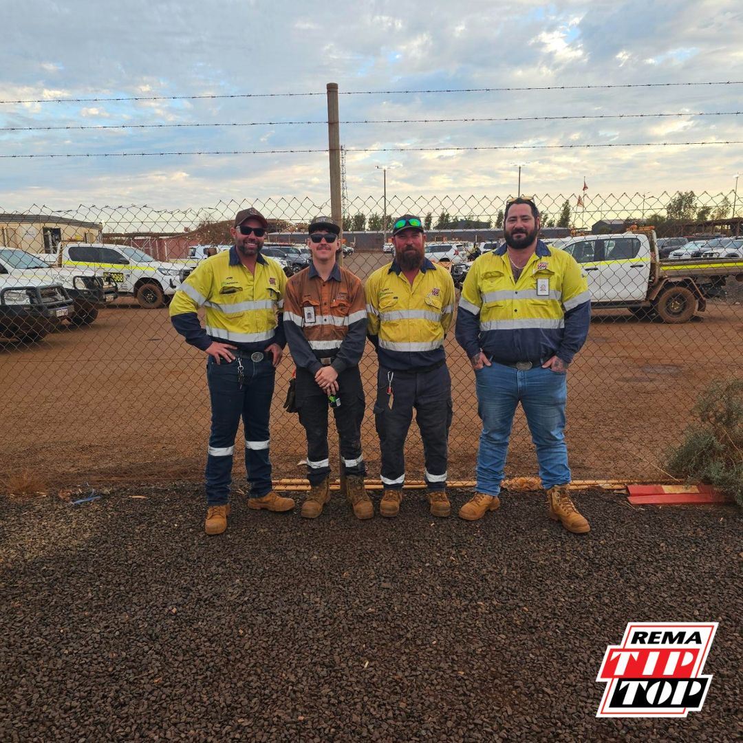 Four workers in high-visibility clothing stand in front of a fence in a gravel lot. Company logo in the corner.